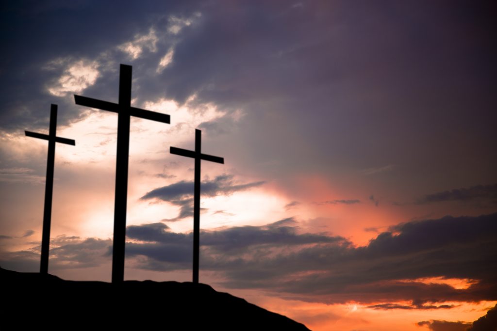 Easter.  The crucifixion.  Three wooden crosses in silhouette stand silently on a hill at sunset.  The dramatic sky is beautiful in its purple and orange colors.  Christianity, religious themes. Copyspace.